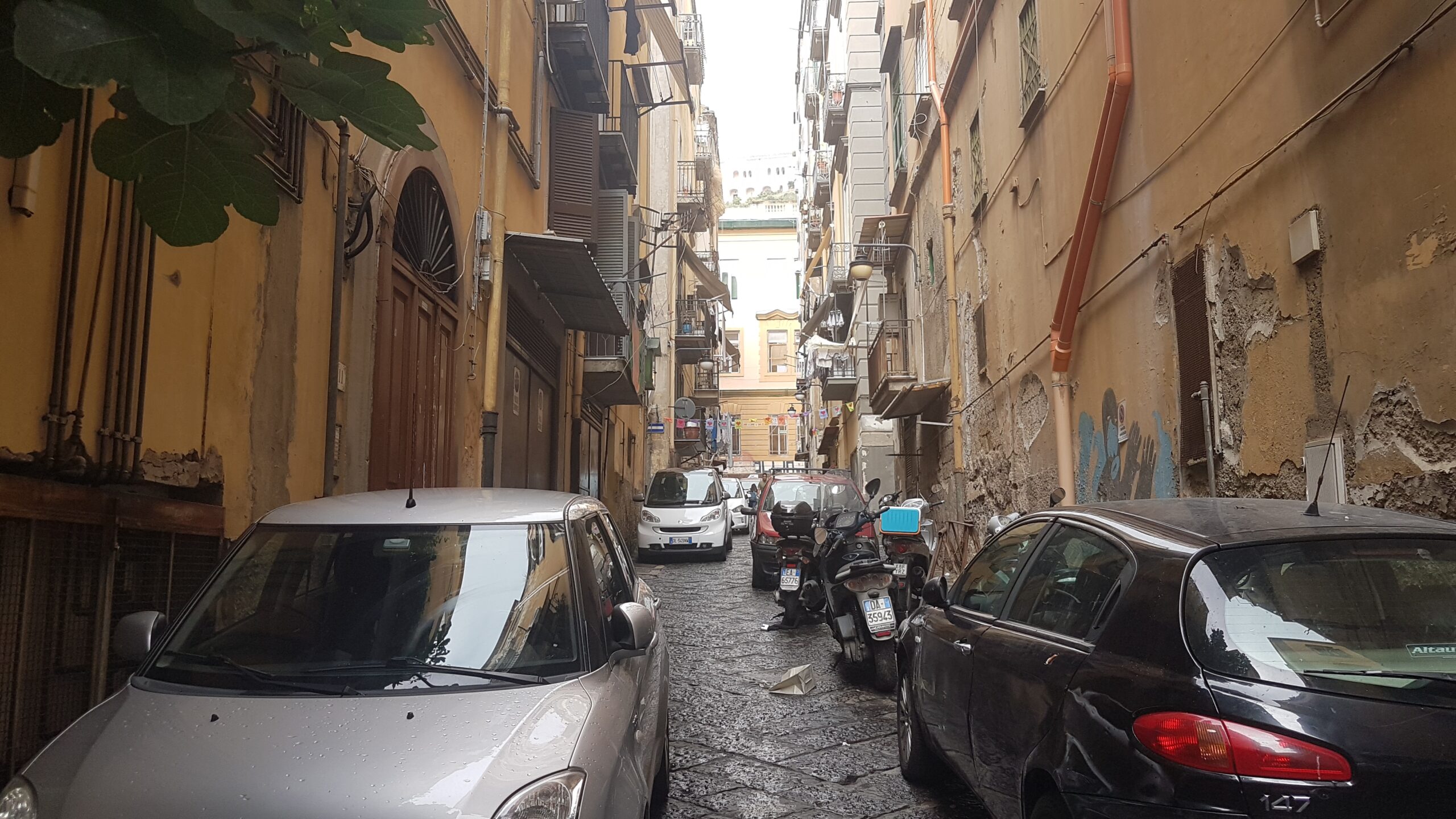 Enge Gasse im historischen Zentrum von Neapel mit parkenden Autos und Rollern